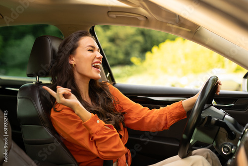 Overjoyed young woman holding auto steering wheel, driving her brand new car and enjoying listening to music, copy space
