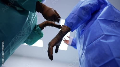 Medical assisting staff holding the gloves. Surgeon shoves his hands into the gloves. Low angle view on the doctor getting ready for operation. photo