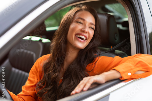 Portrait of young beautiful woman sitting in luxury car looking out of window and smiling, enjoying automobile after test drive