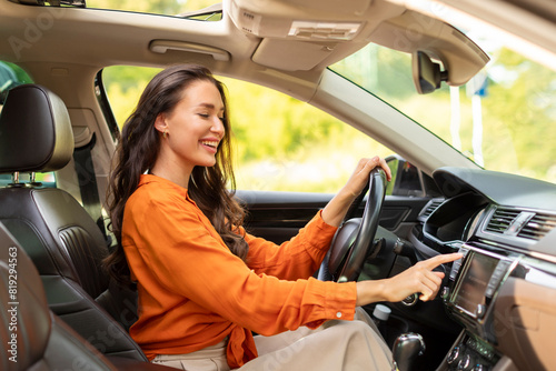 Road playlist. Happy woman driving car and listening to music radio on auto audio system, checking auto options during test drive, pushing button on dashboard © Home-stock