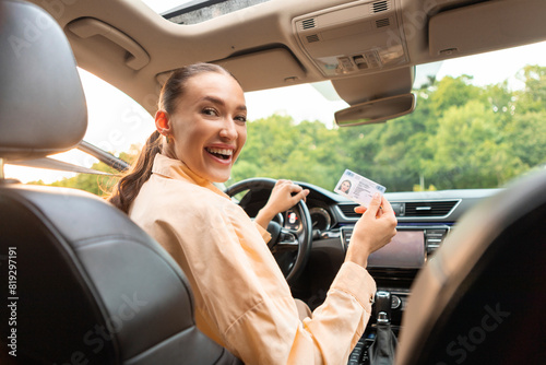 Excited woman sitting in her car and showing new driver license, celebrating driving school finish, passed exam, bought car, sitting inside of vehicle