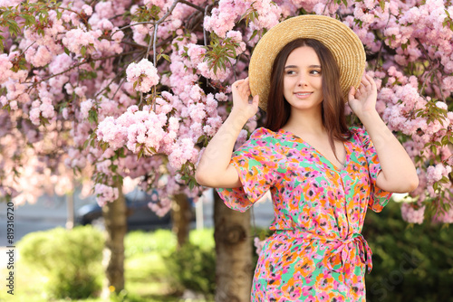 Beautiful woman in straw hat near blossoming tree on spring day