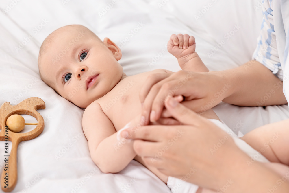 Woman applying body cream onto baby`s skin on bed, closeup Woman applying body cream onto baby`s skin on bed, closeup
