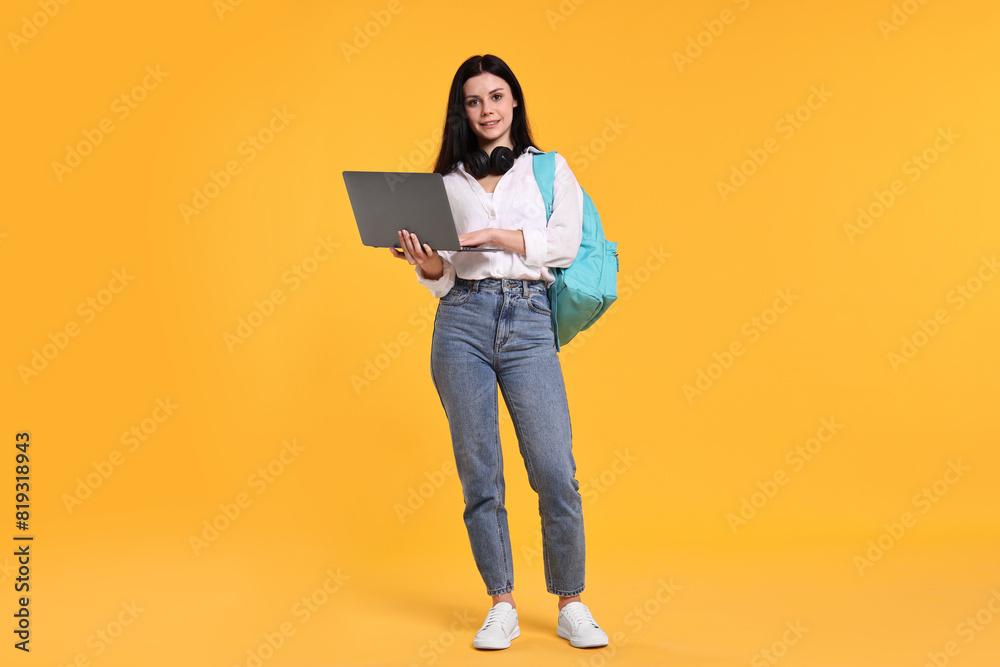 Smiling student with laptop on yellow background
