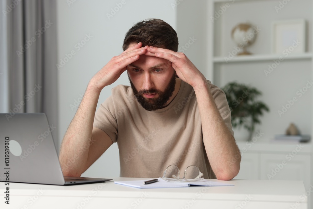 Overwhelmed man sitting with laptop at table indoors Overwhelmed man sitting with laptop at table indoors