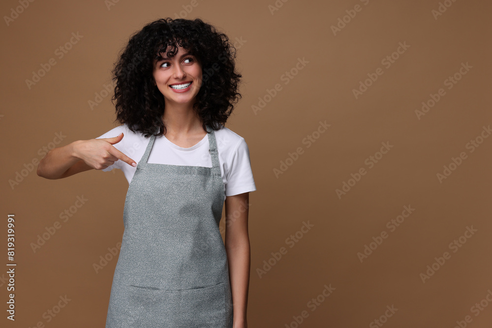 Happy woman pointing at kitchen apron on brown background, space for text. Mockup for design Happy woman pointing at kitchen apron on brown background, space for text. Mockup for design