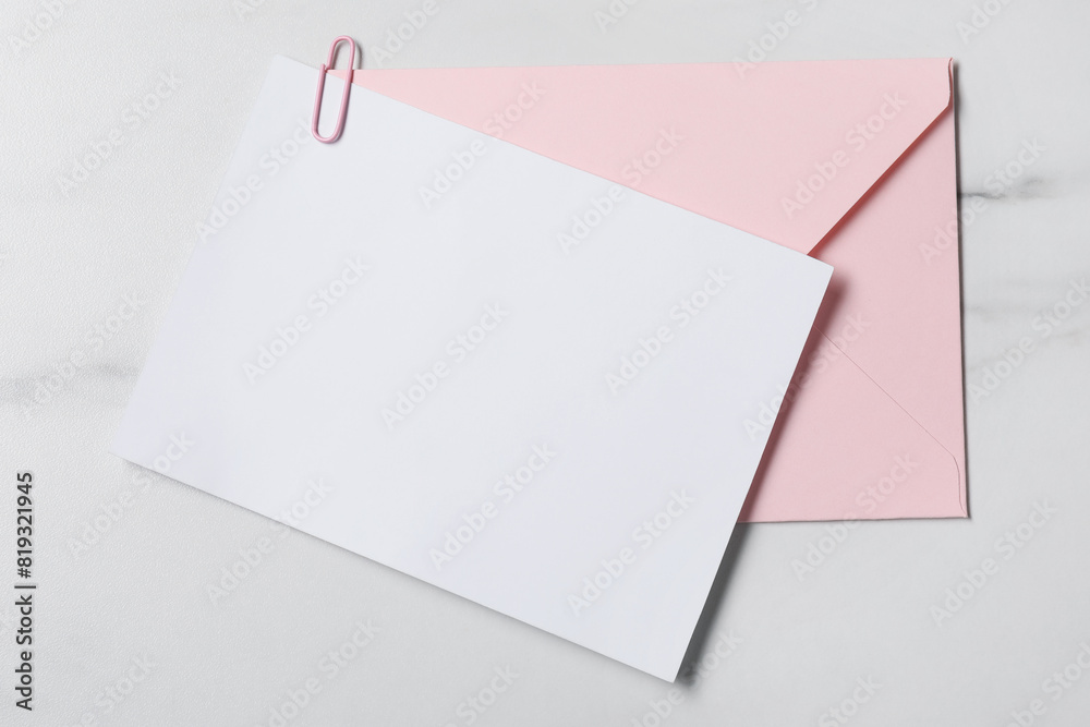 Blank sheet of paper, paperclip and letter envelope on white marble table, top view Blank sheet of paper, paperclip and letter envelope on white marble table, top view