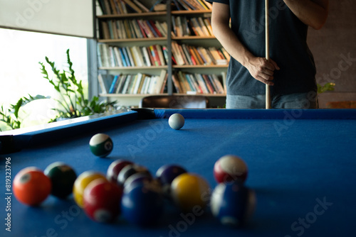 A man is playing billiards in a room with a bookshelf