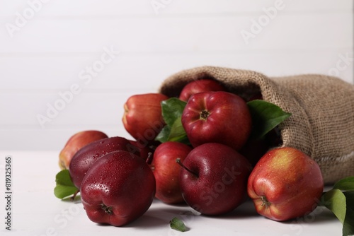 Ripe red apples and green leaves on white table