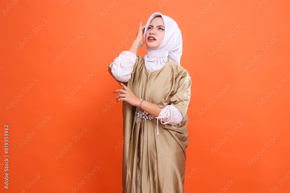 gesture of beautiful adult woman asian candid top sad pain holding her head dizzy wearing kaftan Muslim dress wearing hijab, isolated on orange background. Concept of health care, education, promotion gesture of beautiful adult woman asian candid top sad pain holding her head dizzy wearing kaftan Muslim dress wearing hijab, isolated on orange background. Concept of health care, education, promotion