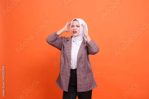 beautiful young indonesia woman wearing a hijab grimacing in pain candid above, Experiencing pain, dizziness, position of both hands on her head with an orange studio.health care, advertising © Ajab