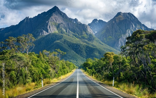 Road stretching towards towering mountains framed by lush forests. © OLGA