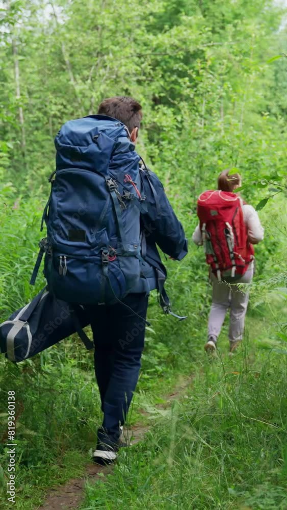 Young couple of hikers walks trying to find perfect spot for nice camping in forest. Young man and woman enjoy hiking together smiling to each other Vertical Shot. Young couple of hikers walks trying to find perfect spot for nice camping in forest. Young man and woman enjoy hiking together smiling to each other Vertical Shot.