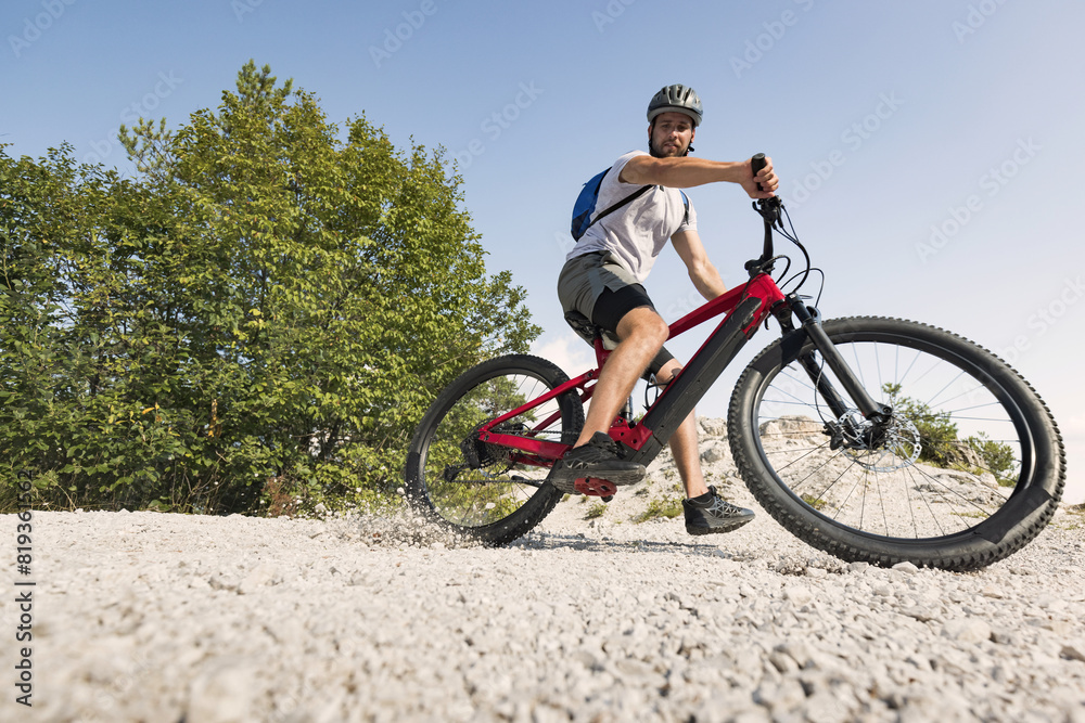 Male electric mountain bike rider going downhill and braking on a hilly rocky trail, low-angle shot. E-mountain biking concept.