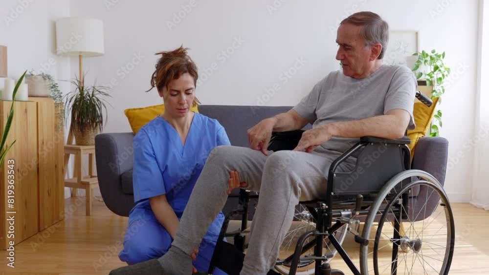 Female medical worker helping senior man in wheelchair doing stretching leg exercises at home. Elderly health care assistance concept. Female medical worker helping senior man in wheelchair doing stretching leg exercises at home. Elderly health care assistance concept.