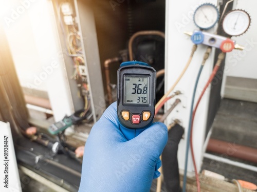 Professional engineer wearing blue gloves using thermo gun for temperature check on the hvac air cinditioning syatem. Temperature check concept on the compressor, condensor , refrigerant system hvac.