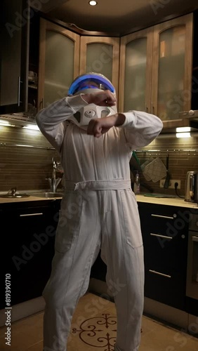 A man in an astronaut costume dances in the kitchen. Funny crazy astronaut is very happy about his future mission to the ISS. Vertical Shot.
