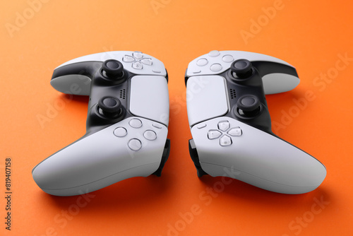 Two wireless game controllers on orange background