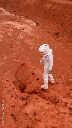 Astronaut looks around crater from asteroid, standing on hill top. Exploring of unknown far planet by NASA concept. Circle drone shot. Vertical Shot.