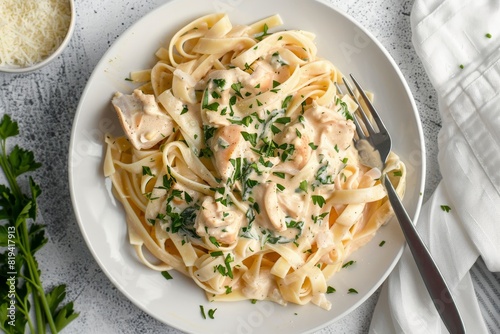 A plate of fettuccine pasta with a smooth, creamy sauce and chopped parsley served on white background