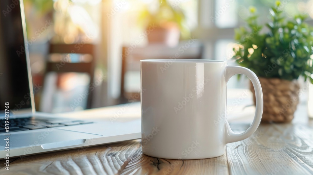A white mug mockup sitting on an office table with a laptop in a blurred background. A coffee cup and computer