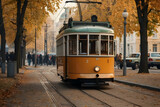 Historical yellow tram moving through an autumnal cityscape with fallen leaves and bystanders