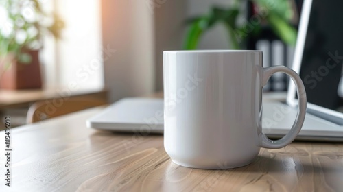 A white mug mockup sitting on an office table with a laptop in a blurred background. A coffee cup and computer