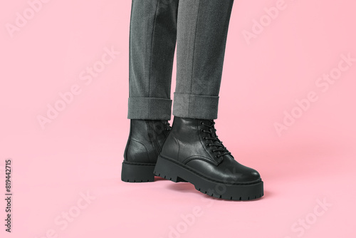 Legs of young woman in stylish black leather boots on pink background