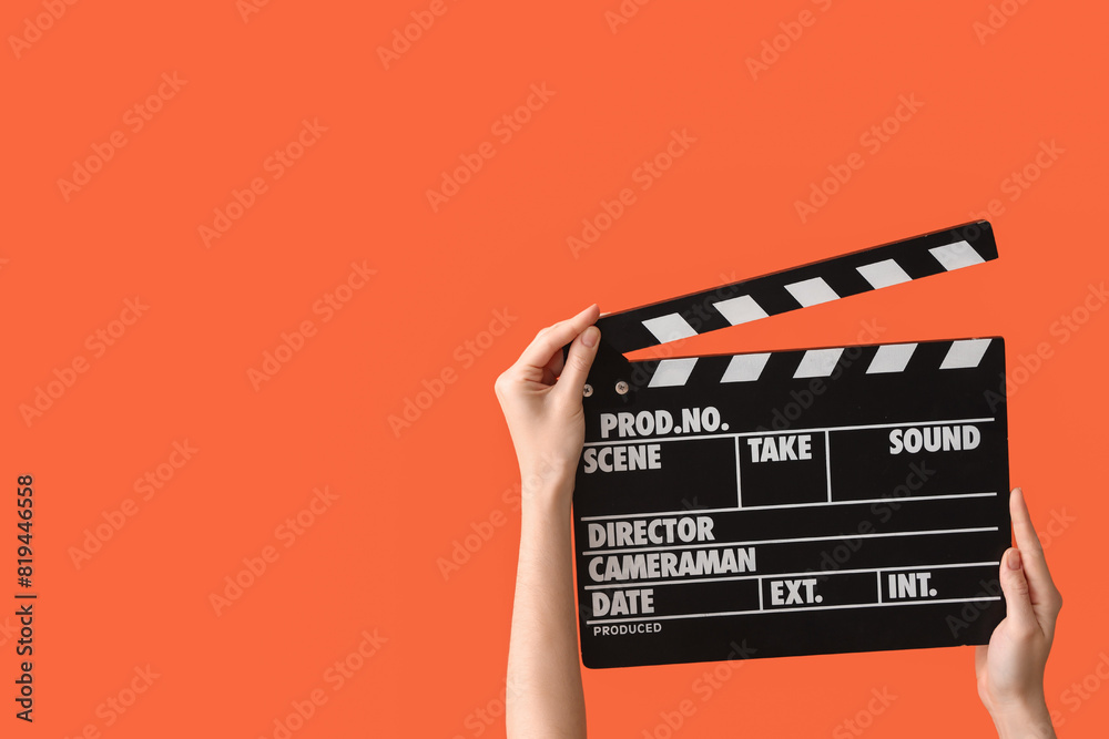 Female hands with movie clapper on orange background