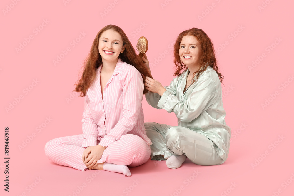 Happy redhead woman brushing her sister's hair on pink background Happy redhead woman brushing her sister's hair on pink background