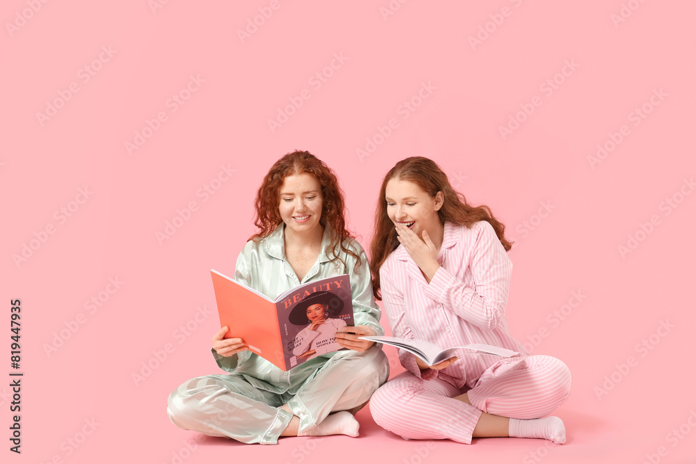 © Pixel-Shot - Happy redhead sisters in pajamas with magazines on pink background