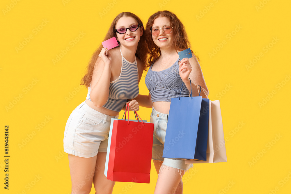 Happy redhead sisters with credit cards and shopping bags on yellow background Happy redhead sisters with credit cards and shopping bags on yellow background
