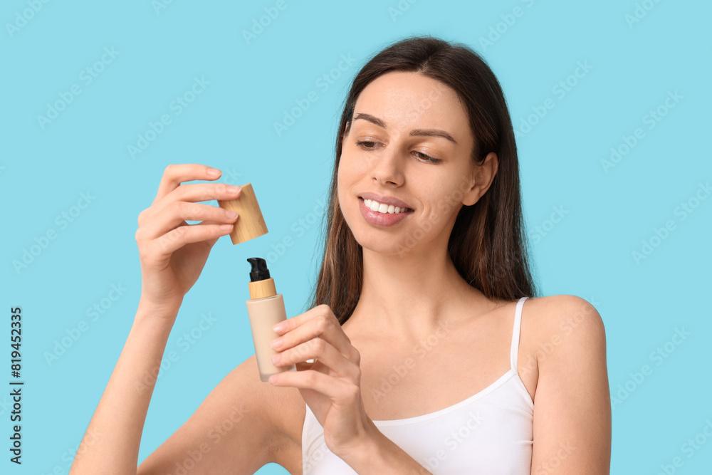 Beautiful young woman opening foundation on blue background Beautiful young woman opening foundation on blue background