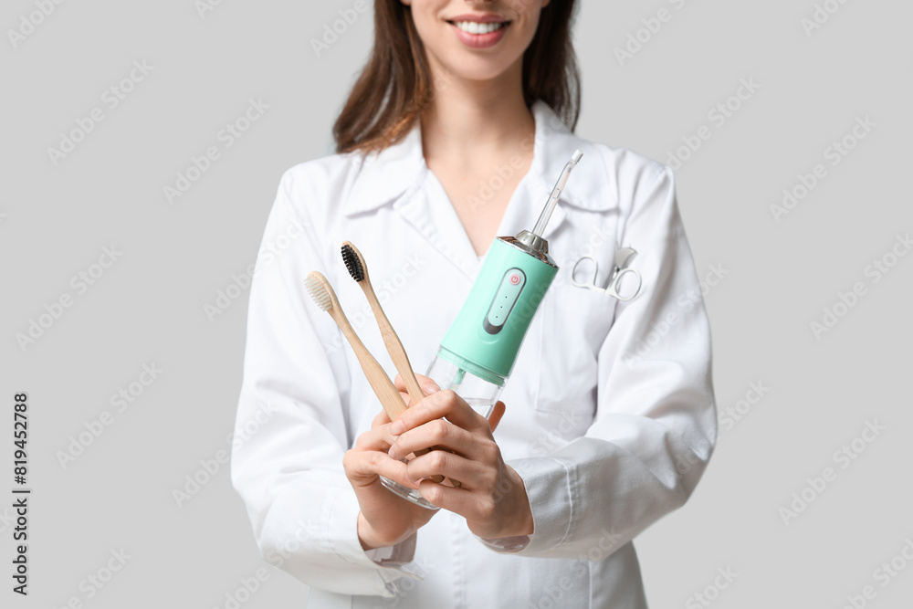 Female dentist with oral irrigator and toothbrushes on grey background Female dentist with oral irrigator and toothbrushes on grey background