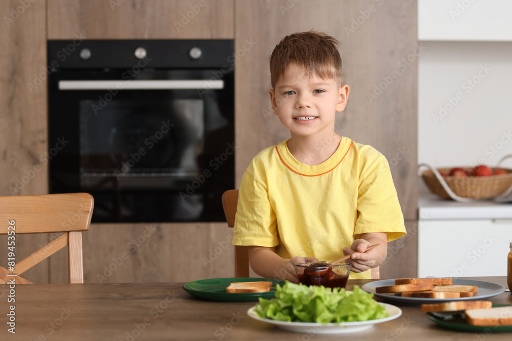 Cute little boy making toast with jam at table in kitchen Cute little boy making toast with jam at table in kitchen