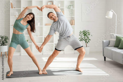 Sporty young couple practicing yoga together in living room photo