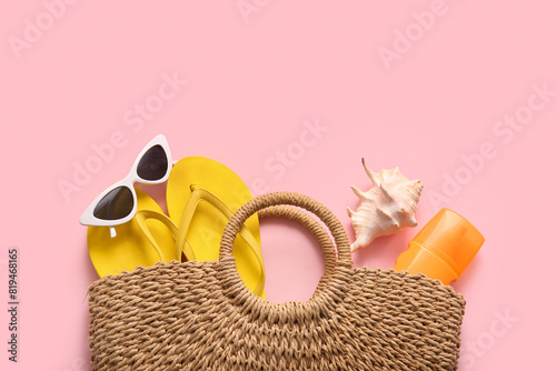 Wicker bag with beach accessories and seashell on pink background