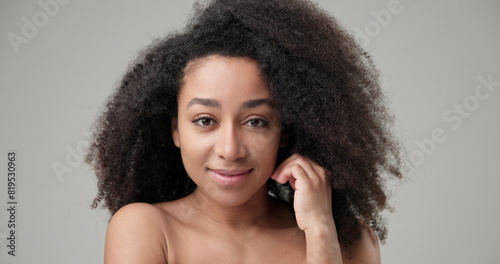 Beauty and healthcare concept - beautiful African American woman with curly afro hairstyle and clean, healthy skin touches her cheek and face with her hand, posing and looking at the camera