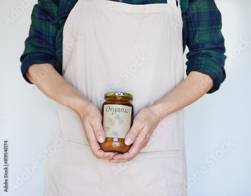 Person, product and hands with organic jam for biodiversity, sustainability and eco friendly in home. Preserver, apron and natural fruit spread for health, quality and wellness on white background photo