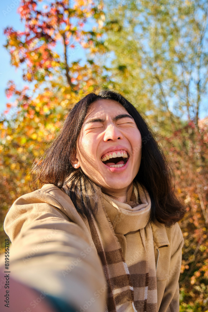Young Asian man with long hair laughing and taking a funny selfie in a park in autumn. Young Asian man with long hair laughing and taking a funny selfie in a park in autumn.