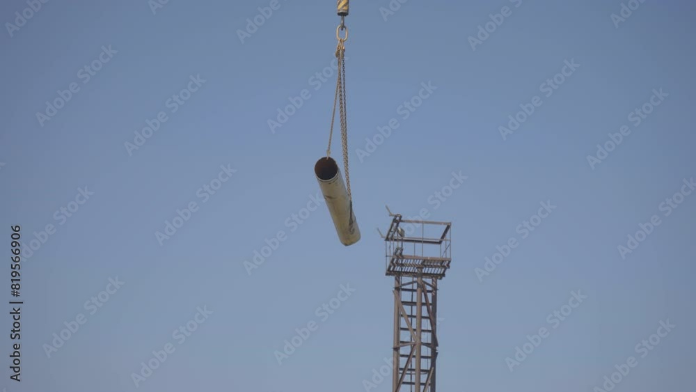 Iron water pipe hanging on hook of crane. Construction process of water pipework in for free flow of water to tanks for further treatment Iron water pipe hanging on hook of crane. Construction process of water pipework in for free flow of water to tanks for further treatment