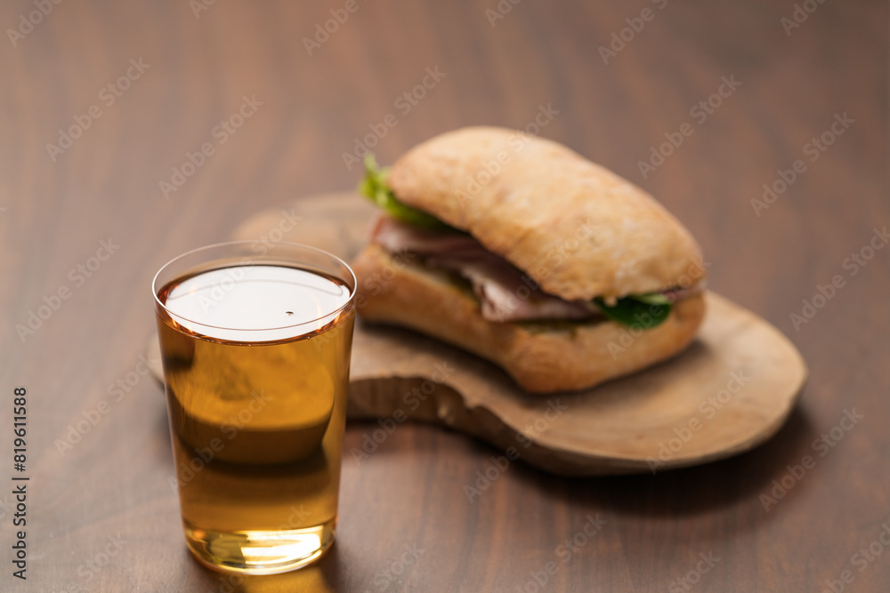Ciabatta sandwich with ham and pesto and glass of cider on wood table Ciabatta sandwich with ham and pesto and glass of cider on wood table