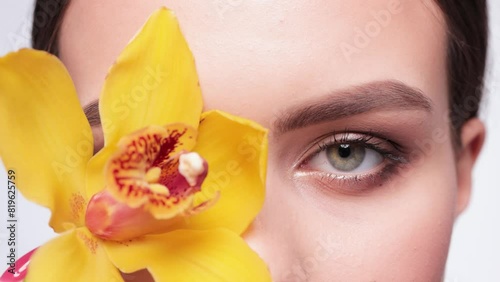 Beautiful green-eyed girl. A girl with a beautiful make-up looks at the camera close-up. She holds a yellow orchid near her eyes. Professional make-up and cosmetic skin care. photo
