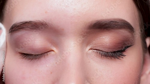 A young beautiful girl removes makeup with a cotton pad and micellar water from her face and eyes.