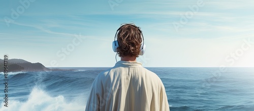 A man in a bathrobe and earphones with slouched shoulders gazes thoughtfully at the ocean waves with the horizon ahead creating a contemplative scene in the copy space image photo