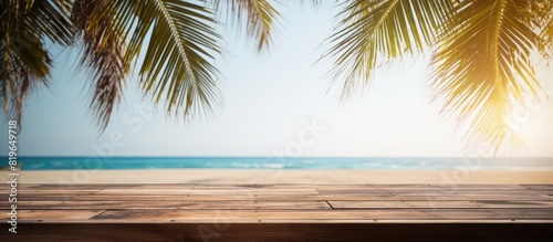 Wooden planks with a blurred beach in the background are suitable for product placement with palm leaves in the foreground providing copy space image opportunity