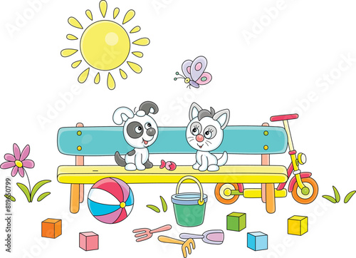 Happy little puppy and kitten sitting on a small bench among scattering toys in a park and playing with a merrily fluttering butterfly on a sunny summer day, vector cartoon illustration on white