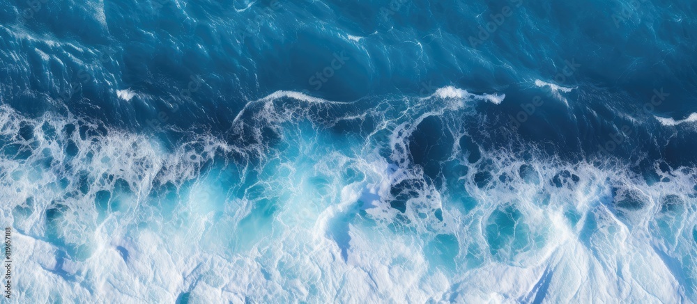An impressive ocean background featuring a striking contrast between deep blue sea and foamy white waves when viewed from above with copy space image
