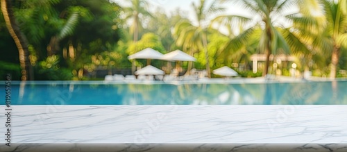 A white marble table with ample copy space image overlooking a blurred sunny pool in a tropical resort perfect for showcasing or editing your products