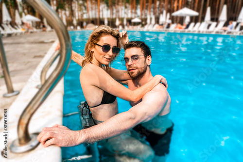 Young romantic couple in stylish sunglasses posing for the camera in an outdoor swimming pool. Romance and summer vacation concept